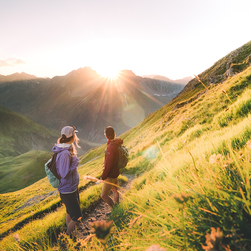 Wanderer genießen Sonnenaufgang in den Bergen bei St. Anton am Arlberg mit Blick ins Tal