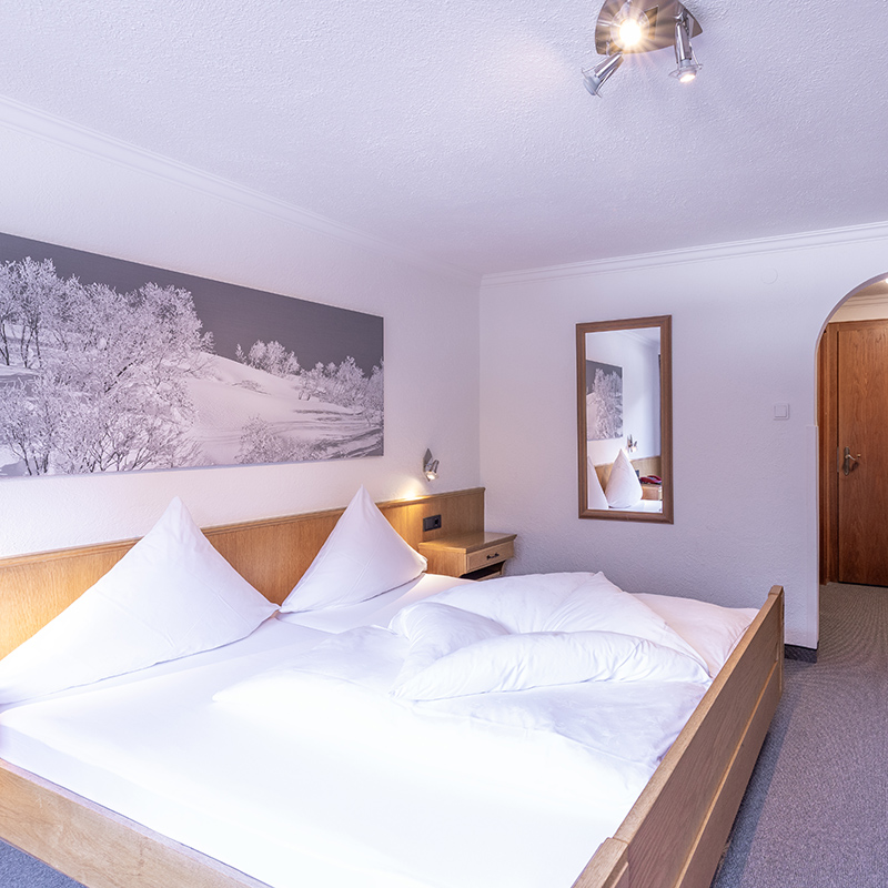 Helles Doppelzimmer im Hotel Garni Bergwelt mit gemütlichem Bett, Holzmöbeln und alpinem Wandbild